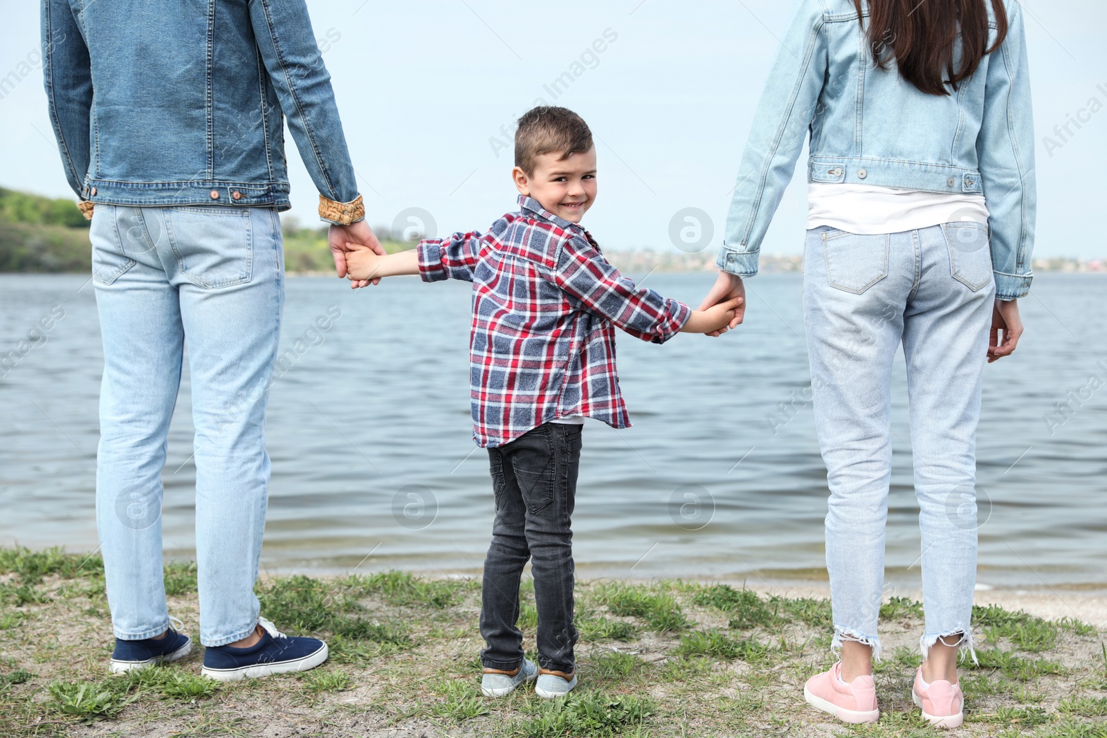 Photo of Cute little child holding hands with his parents near river. Family time