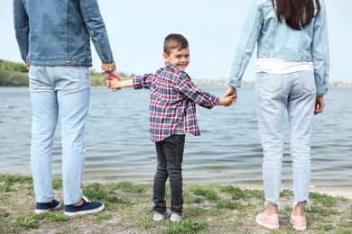 Cute little child holding hands with his parents near river. Family time