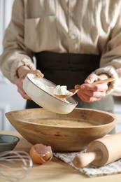 Making dough. Woman adding flour into bowl at wooden table in kitchen, closeup