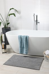 Stylish bathroom interior with bath tub, houseplant and soft light grey mat