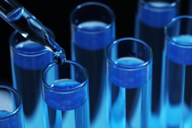Dripping reagent into test tube with blue liquid on black background, closeup. Laboratory analysis