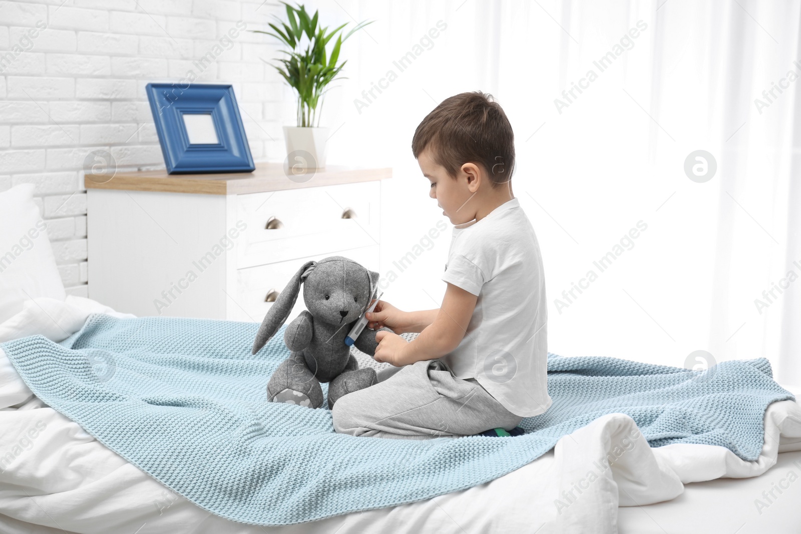 Photo of Cute child playing doctor with stuffed toy on bed in hospital ward