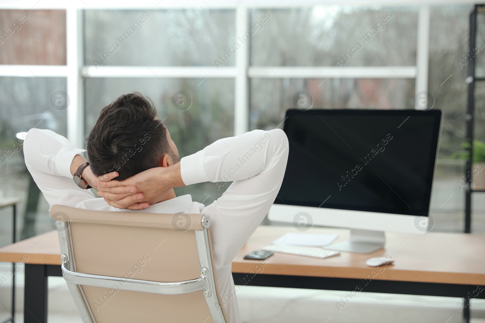 Photo of Young businessman relaxing in office chair at workplace, back view. Space for text