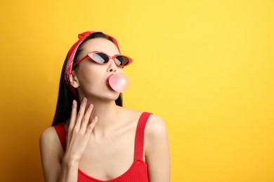 Photo of Fashionable young woman in pin up outfit blowing bubblegum on yellow background, space for text