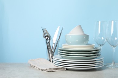 Beautiful ceramic dishware, glasses and cutlery on light grey table, space for text