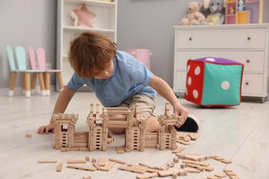 Photo of Little boy playing with wooden construction set on floor in room. Child's toy