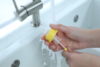 Photo of Woman washing baby bottle nipple under stream of water, closeup