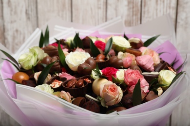 Photo of Beautiful bouquet of flowers and chocolate candies on white wooden background, closeup