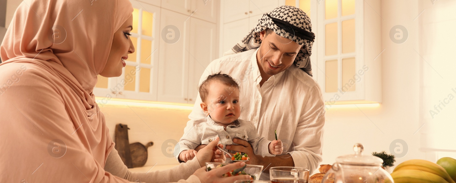 Image of Happy Muslim family with little son at served table in kitchen. Banner design 