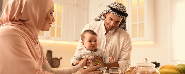 Happy Muslim family with little son at served table in kitchen. Banner design 