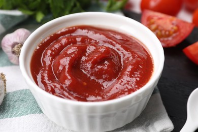 Photo of Organic ketchup in bowl on black table, closeup. Tomato sauce