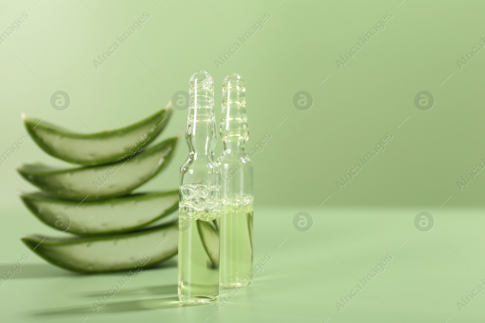 Photo of Skincare ampoules with extract of aloe vera and cut leaves on pale green background, closeup. Space for text