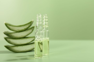 Skincare ampoules with extract of aloe vera and cut leaves on pale green background, closeup. Space for text