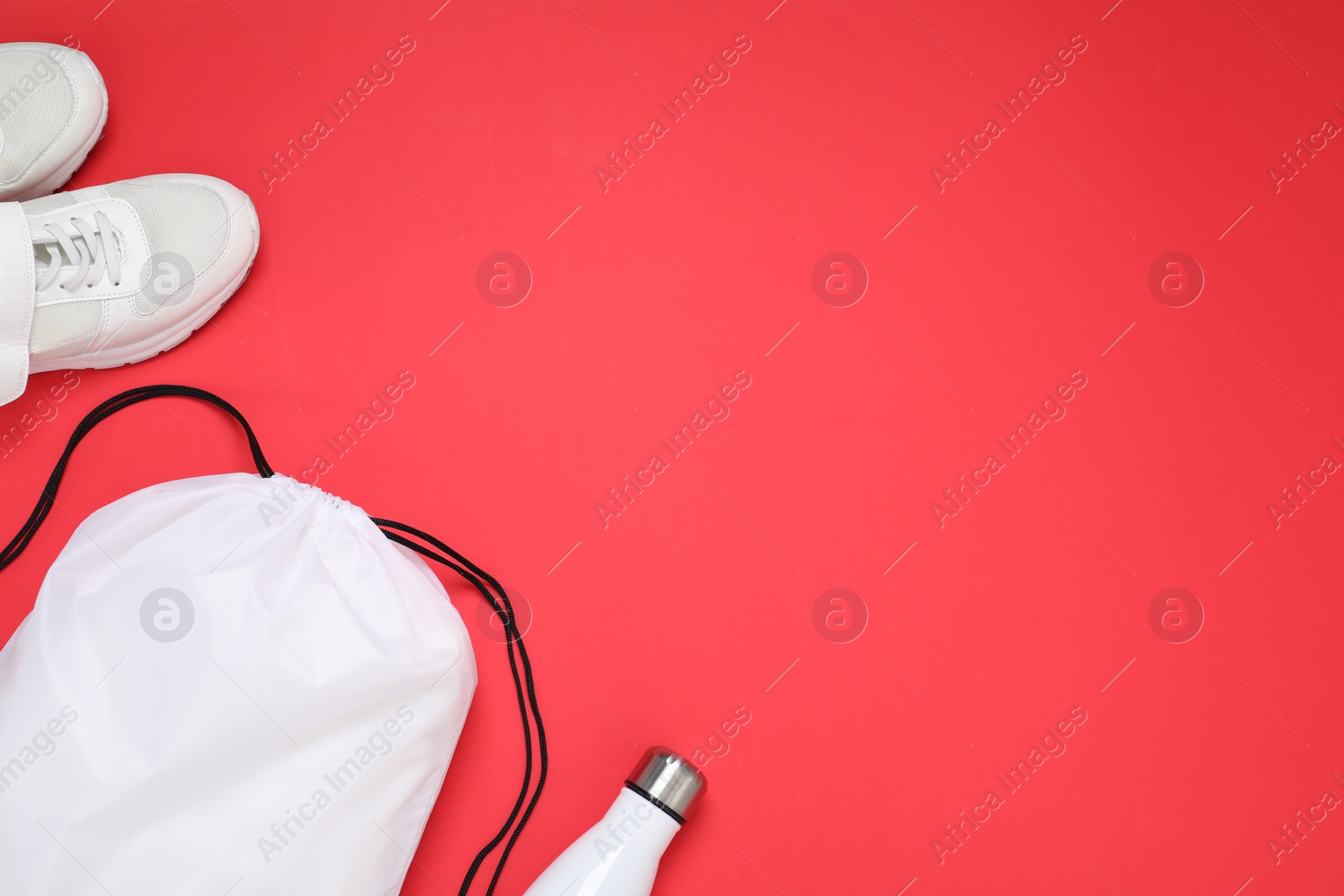 Photo of White drawstring bag, thermo bottle and sneakers on red background, flat lay. Space for text