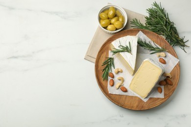 Plate with pieces of tasty camembert cheese, nuts, olives and rosemary on white marble table, flat lay. Space for text