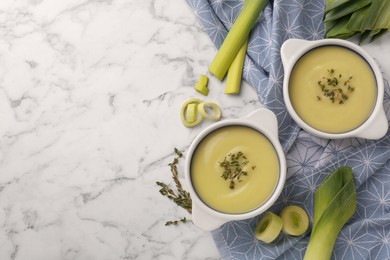 Photo of Tasty leek soup in bowls on white marble table, flat lay. Space for text