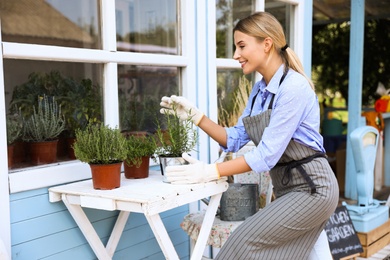 Photo of Young woman taking care of home plants at white wooden table outdoors