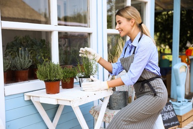 Young woman taking care of home plants at white wooden table outdoors