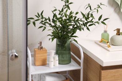 Photo of Vase with green branches and different toiletries on rack in bathroom