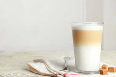 Photo of Delicious latte macchiato and sugar cubes on white wooden table indoors, space for text
