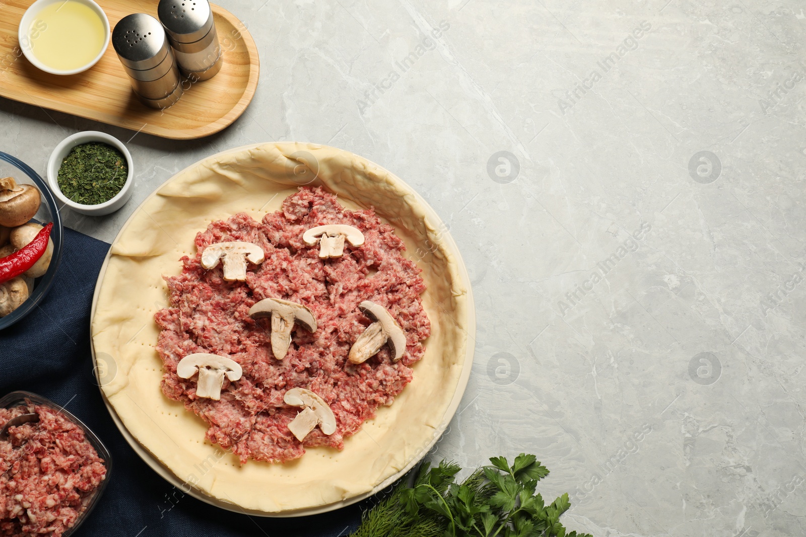 Photo of Flat lay composition with raw dough and ingredients on light grey table, space for text. Baking meat pie