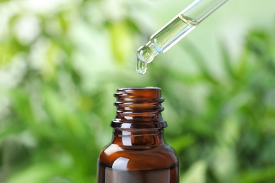 Dropping essential oil into glass bottle on blurred background, closeup