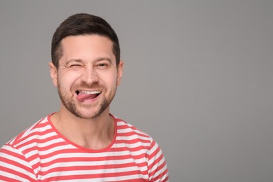 Happy man showing his tongue and winking on grey background. Space for text