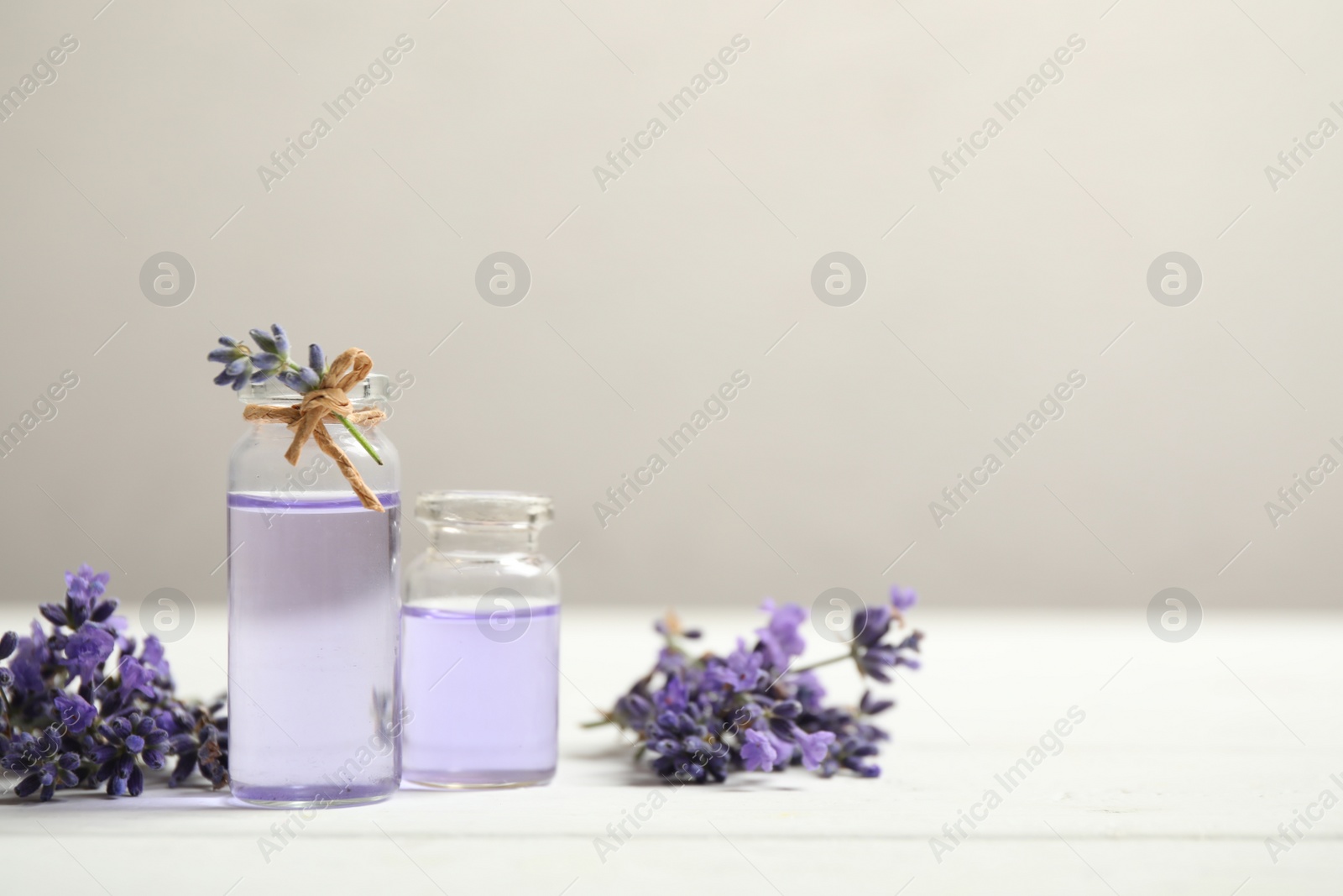 Photo of Bottles of essential oil and lavender flowers on white wooden table. Space for text