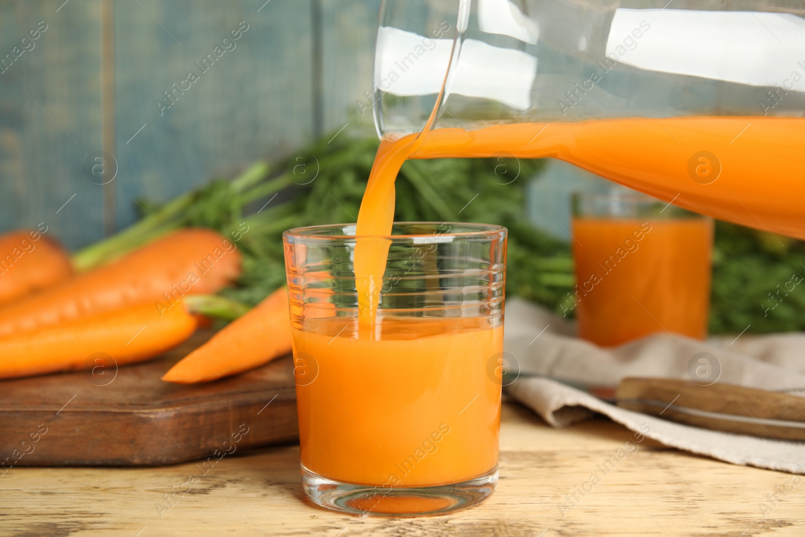 Photo of Pouring freshly made carrot juice into glass on wooden table