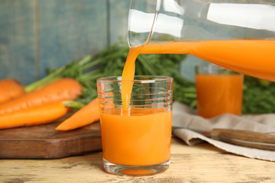 Photo of Pouring freshly made carrot juice into glass on wooden table