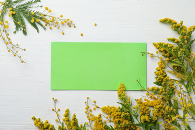 Photo of Green card and fresh mimosa flowers on white wooden table, flat lay. Space for text