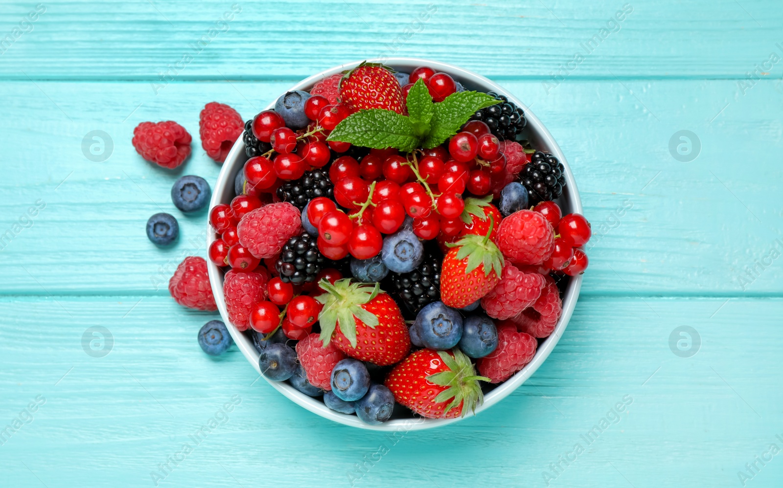 Photo of Mix of different fresh berries and mint in bowl on light blue wooden table, flat lay