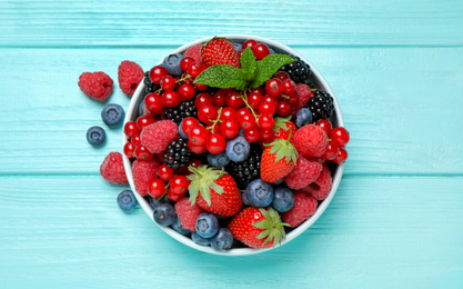 Mix of different fresh berries and mint in bowl on light blue wooden table, flat lay