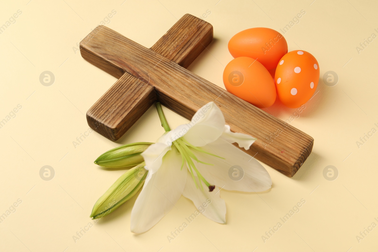 Photo of Wooden cross, painted Easter eggs and lily flowers on pale yellow background