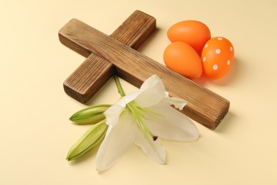 Wooden cross, painted Easter eggs and lily flowers on pale yellow background