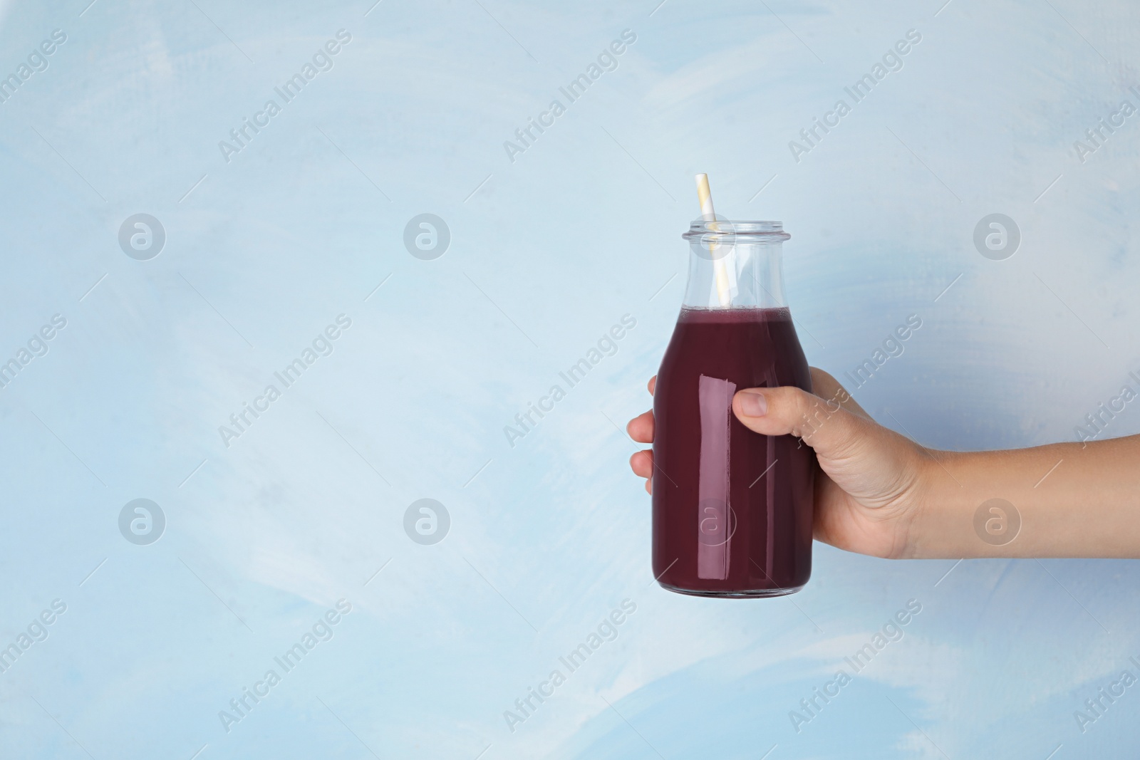 Photo of Woman with bottle of fresh acai drink and straw on light blue background, closeup. Space for text