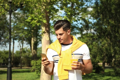 Handsome man with smartphone and refreshing drink in park