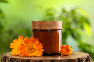 Photo of Jar of cosmetic product and beautiful calendula flowers on wooden stump outdoors