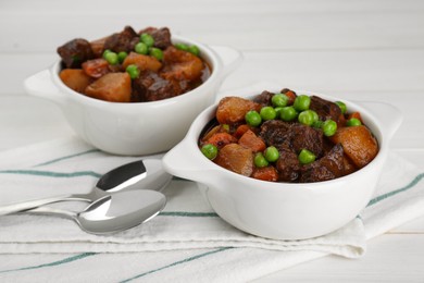 Delicious beef stew with carrots, peas and potatoes on white wooden table, closeup