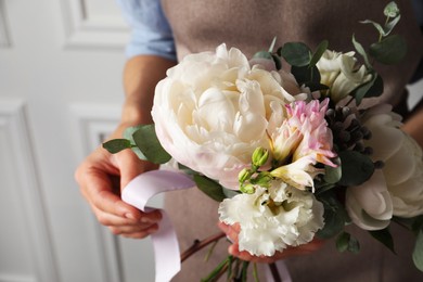 Florist creating beautiful bouquet at white wall, closeup