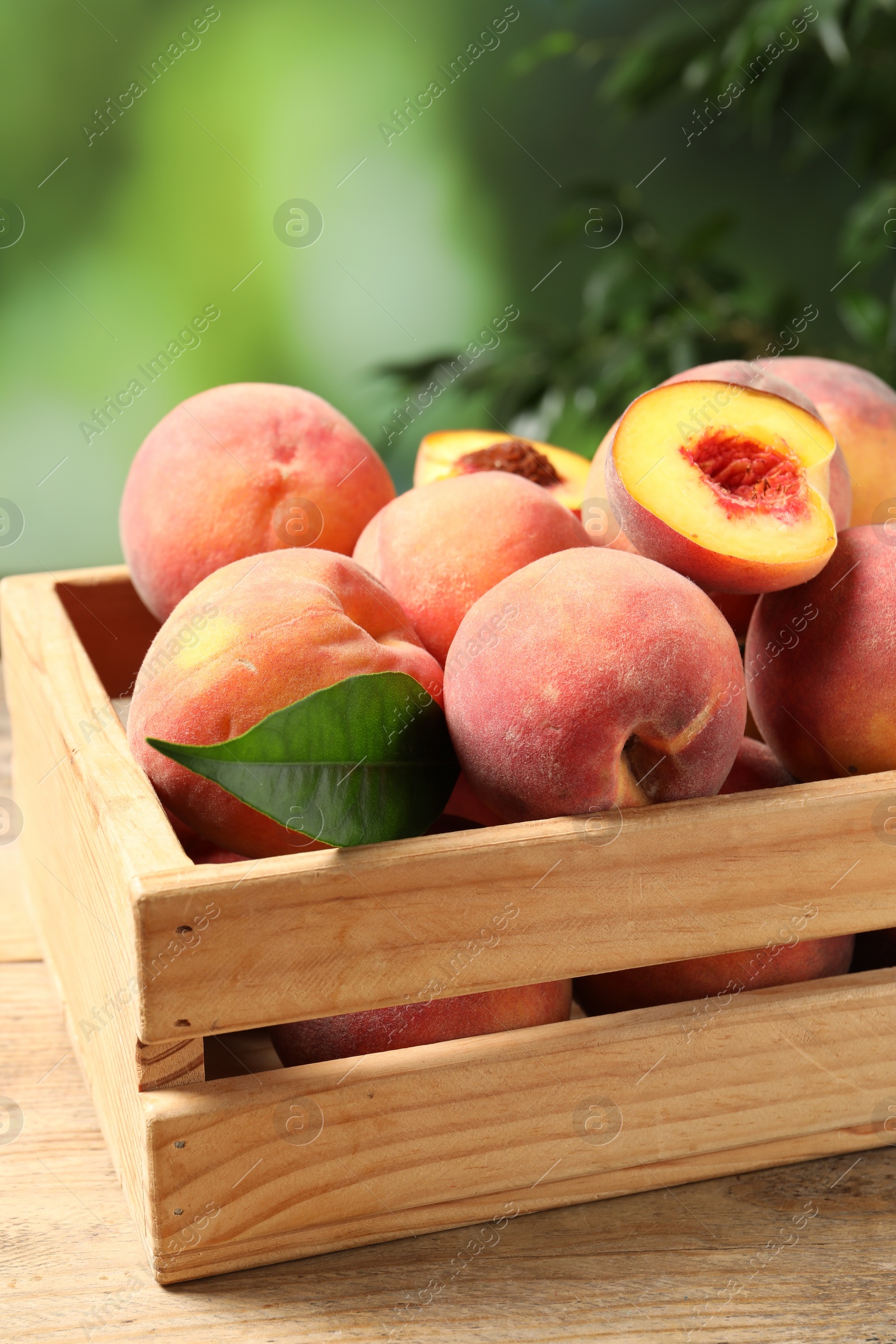 Photo of Cut and whole fresh ripe peaches in crate on wooden table against blurred background, closeup