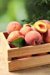 Photo of Cut and whole fresh ripe peaches in crate on wooden table against blurred background, closeup