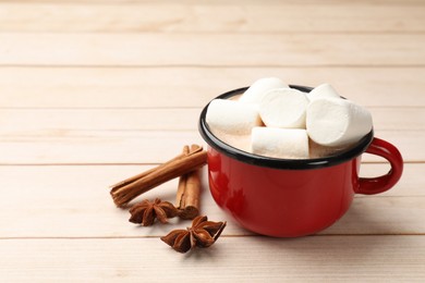 Photo of Tasty hot chocolate with marshmallows and spices on light wooden table, closeup. Space for text