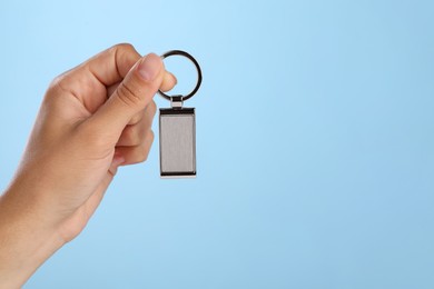 Woman holding metallic keychain on light blue background, closeup. Space for text