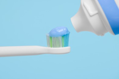 Photo of Electric toothbrush with paste on light blue background, closeup