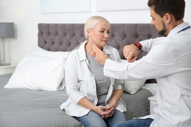 Doctor checking mature woman's pulse with fingers in bedroom