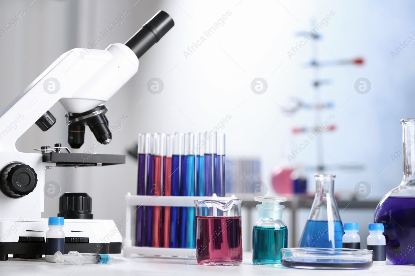 Photo of Different glassware with samples and microscope on table in chemistry laboratory