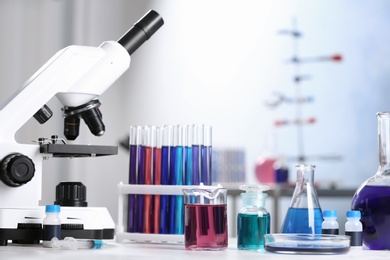 Photo of Different glassware with samples and microscope on table in chemistry laboratory