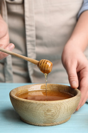 Photo of Woman with honey and dipper at blue wooden table, closeup