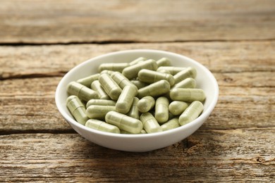 Photo of Vitamin capsules in bowl on wooden table, closeup